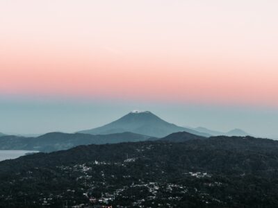 An aerial photograph of Los Planes de Renderos, overlooking San Salvador. It is dusk, with a pink and blue gradient in the sky.
